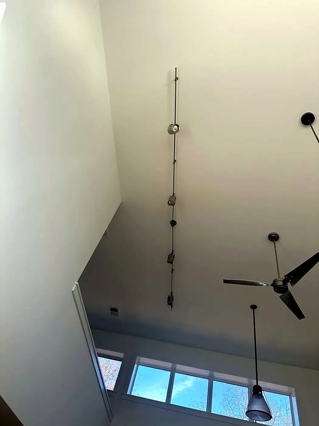Two black ceiling fans on long downrods in a tall white room with track lights and a pendant