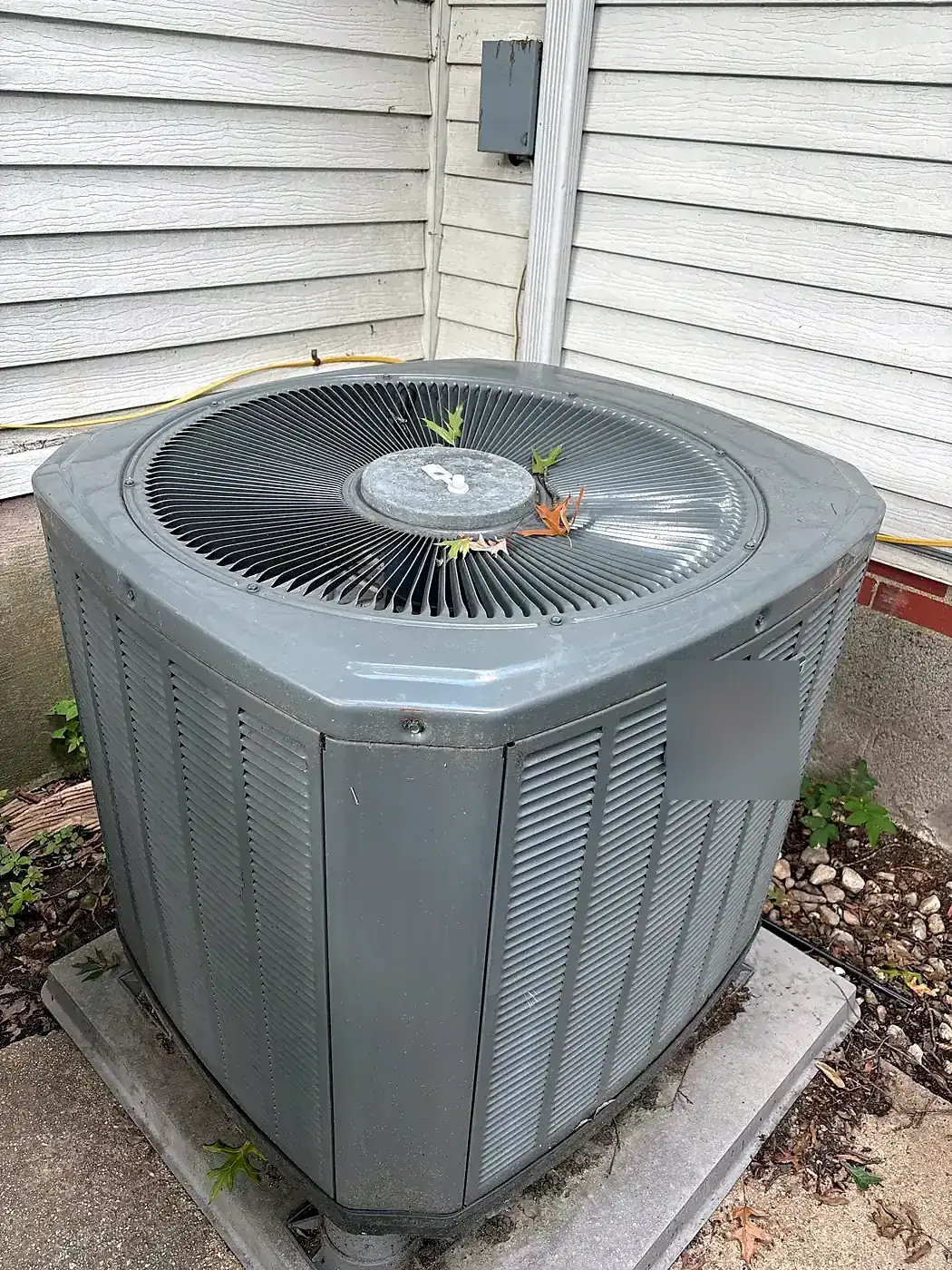 Large gray AC condenser on a fresh concrete pad at the corner of a house with gray vinyl siding