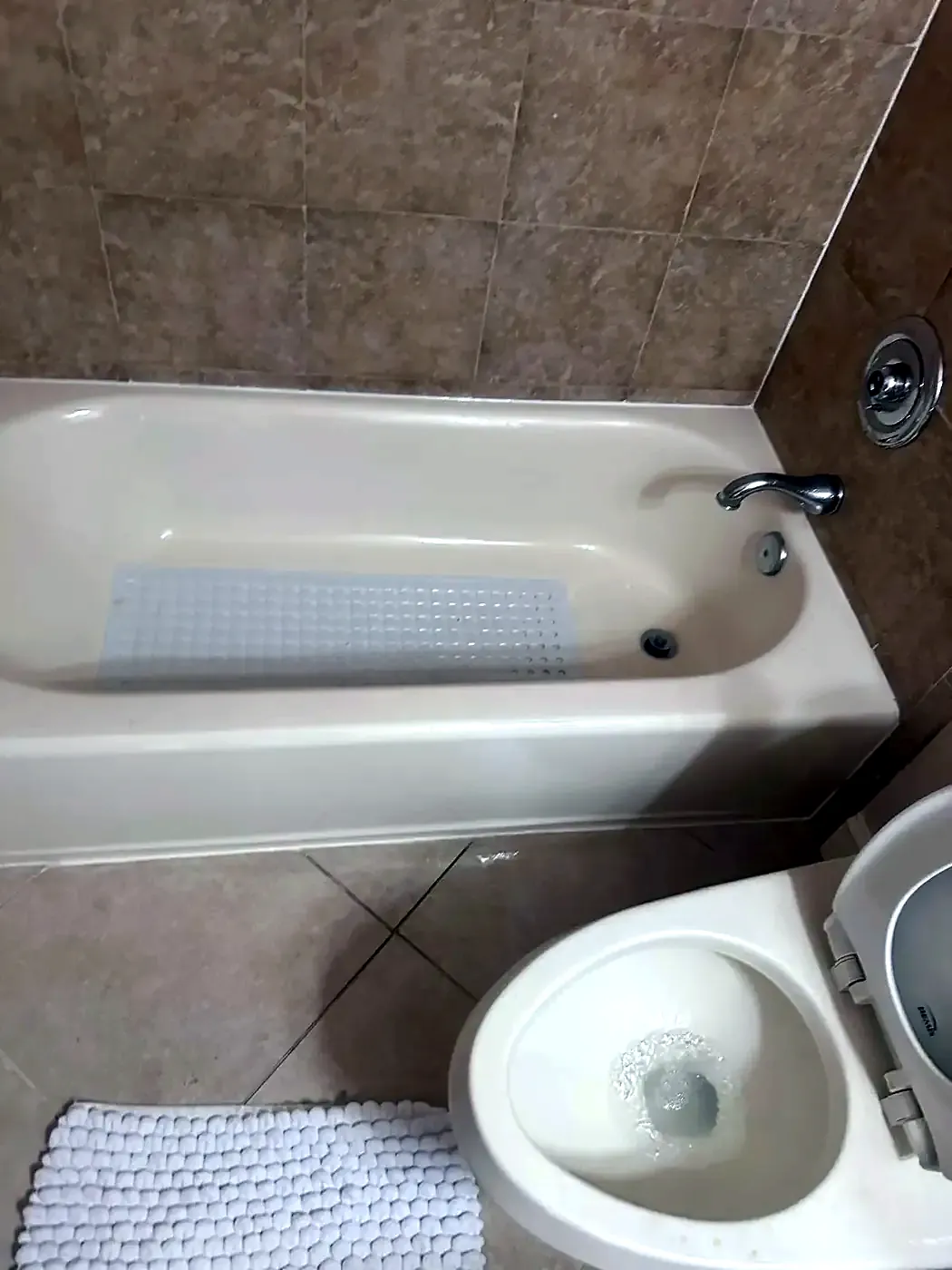 Older beige tub and tile surround with a toilet alongside, before recaulking
