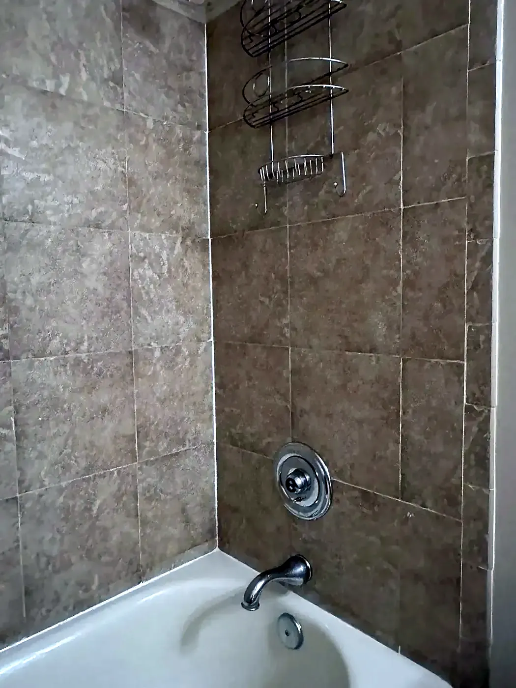 Tub and shower with brown marble-look tile and chrome fixtures, fresh caulk along the tub rim