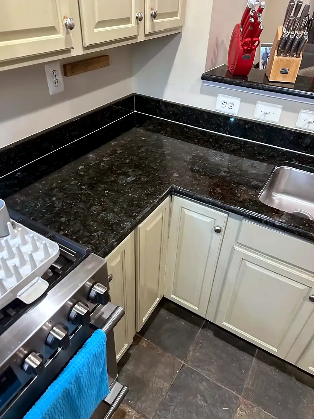 Kitchen with dark granite counters and cream cabinets, caulk seam along the backsplash