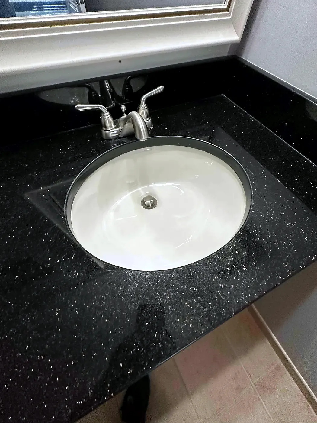 Brushed nickel two-handle faucet over a white oval sink set in a black speckled granite vanity top
