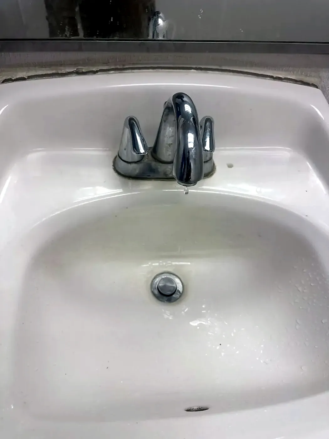 Old chrome single-handle bathroom faucet with a worn, pitted finish on a white sink