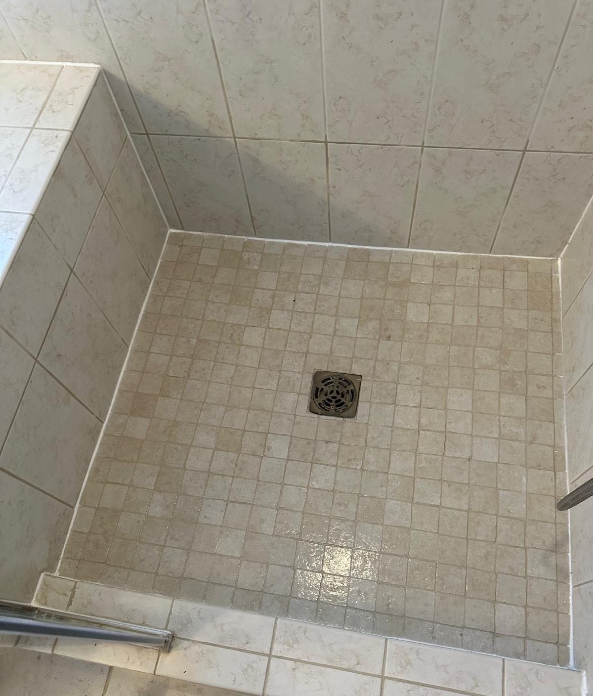 The same shower pan after re-grouting, with clean joints and a fresh caulk line at the walls