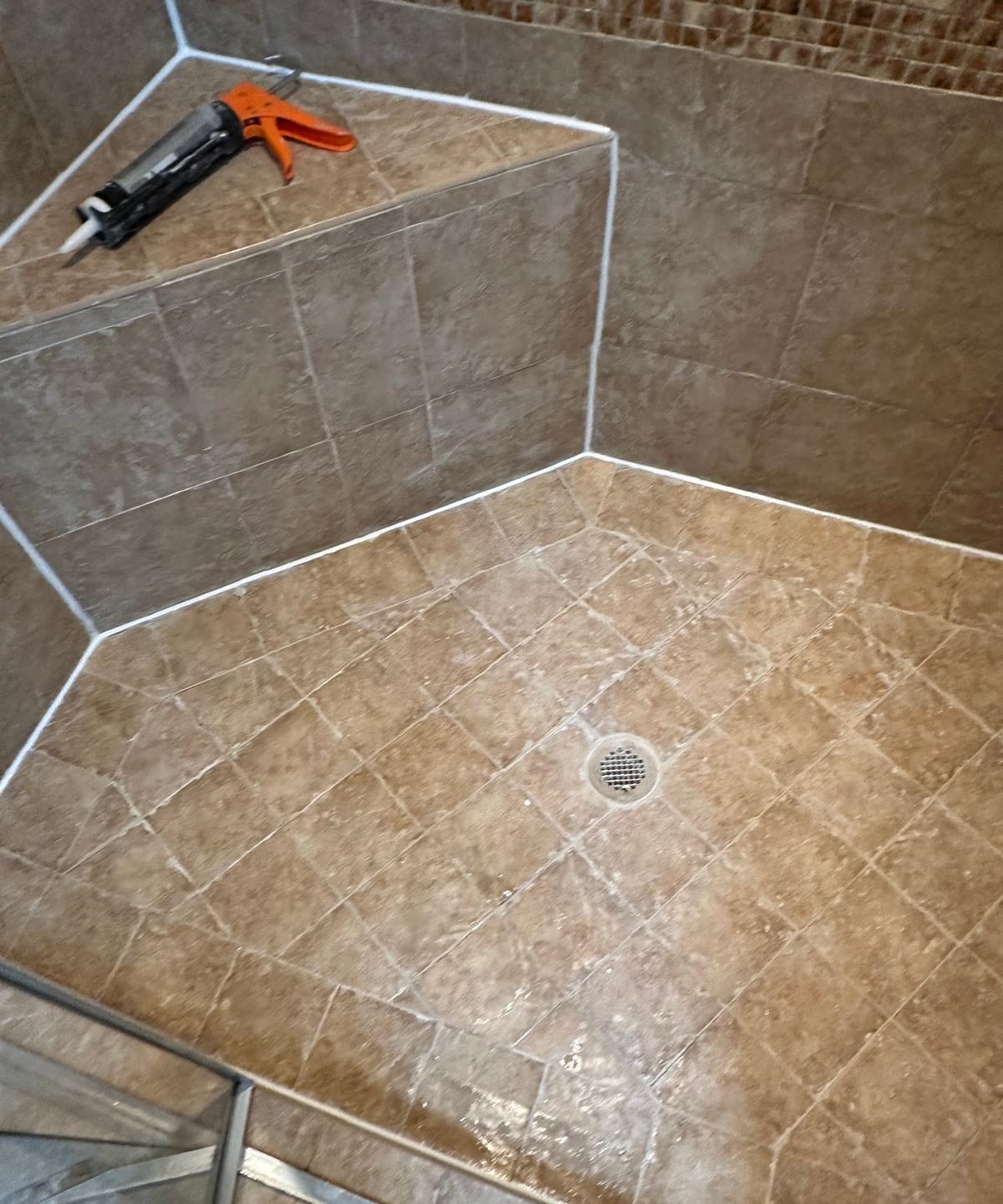 The same shower pan re-grouted, with fresh white caulk lines run into every corner