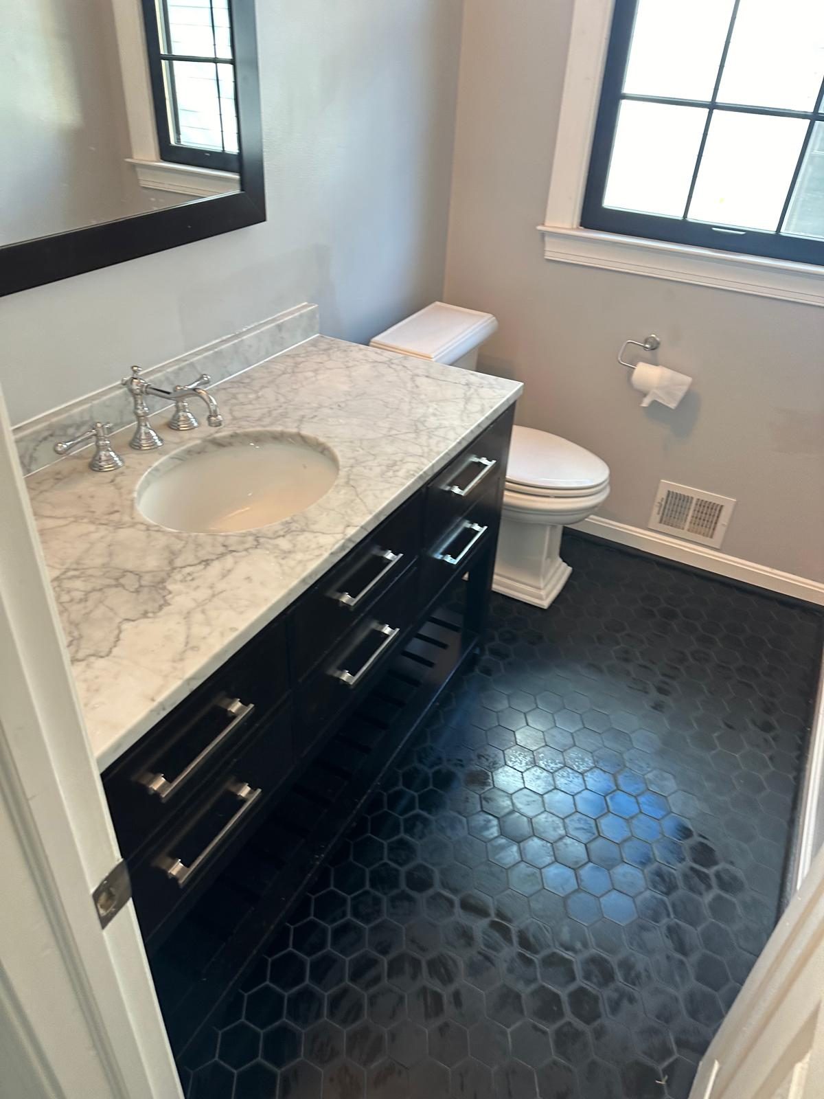 Finished powder room with hexagon tile floor, dark vanity and marble countertop