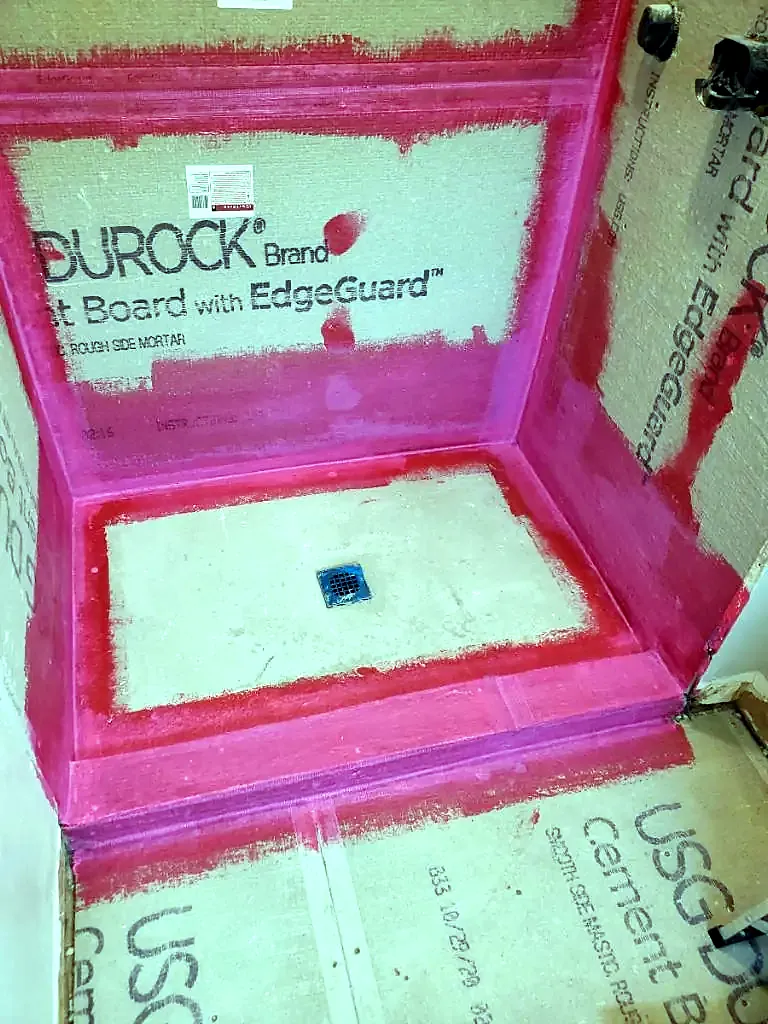 Shower pan and curb coated in red waterproofing over cement board walls, square drain in the center