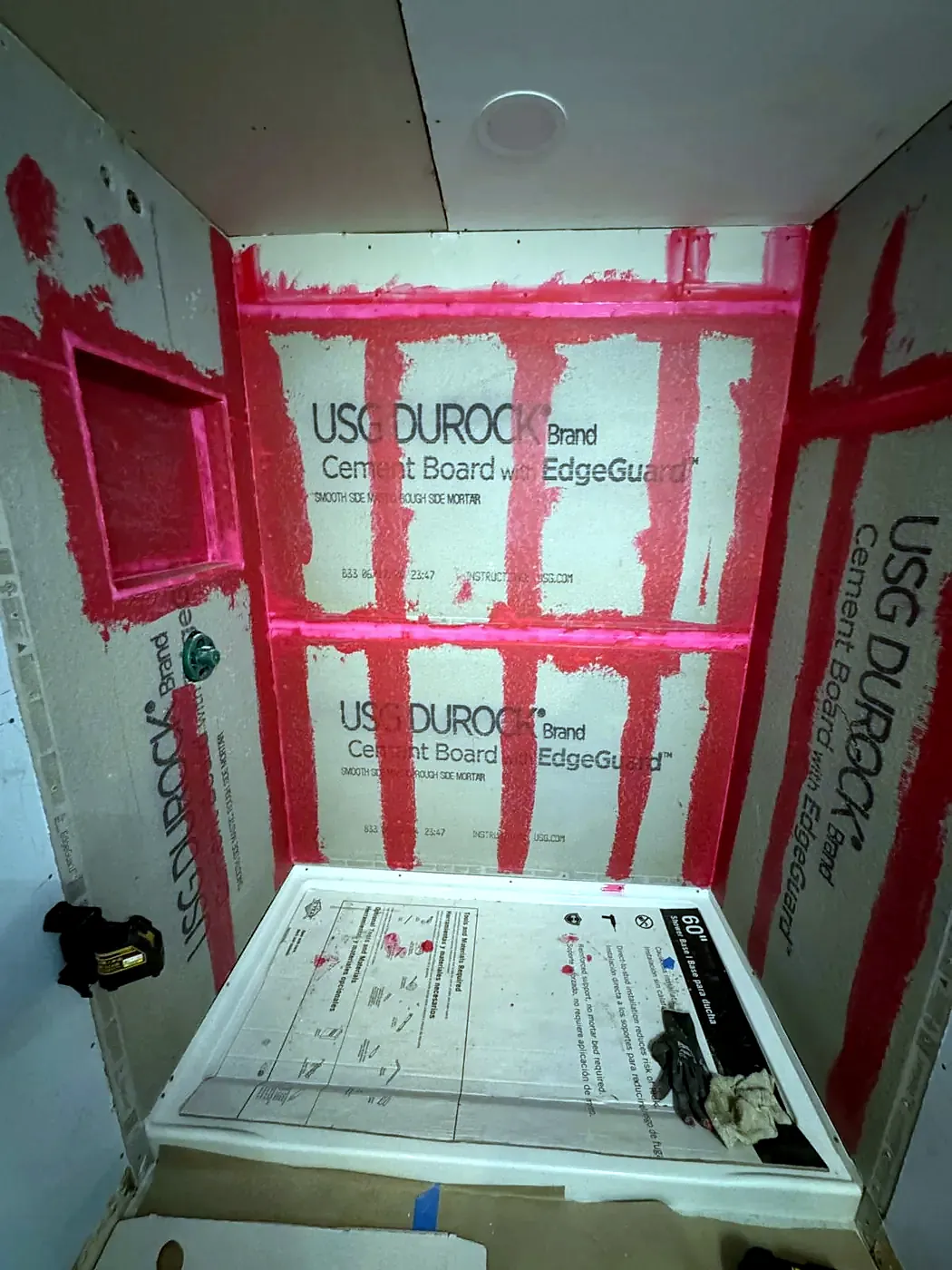 Shower stall with cement board walls, red-sealed seams and a wall niche before tile, shower base on the floor