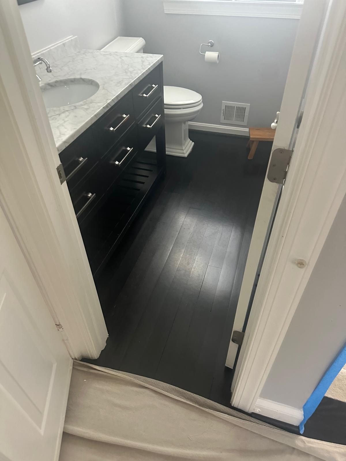 Powder room seen from the doorway before work, with worn dark hardwood flooring