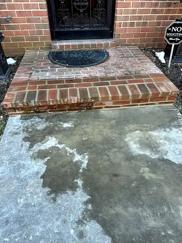 Brick landing at a front door with a black iron storm door and a half-round doormat