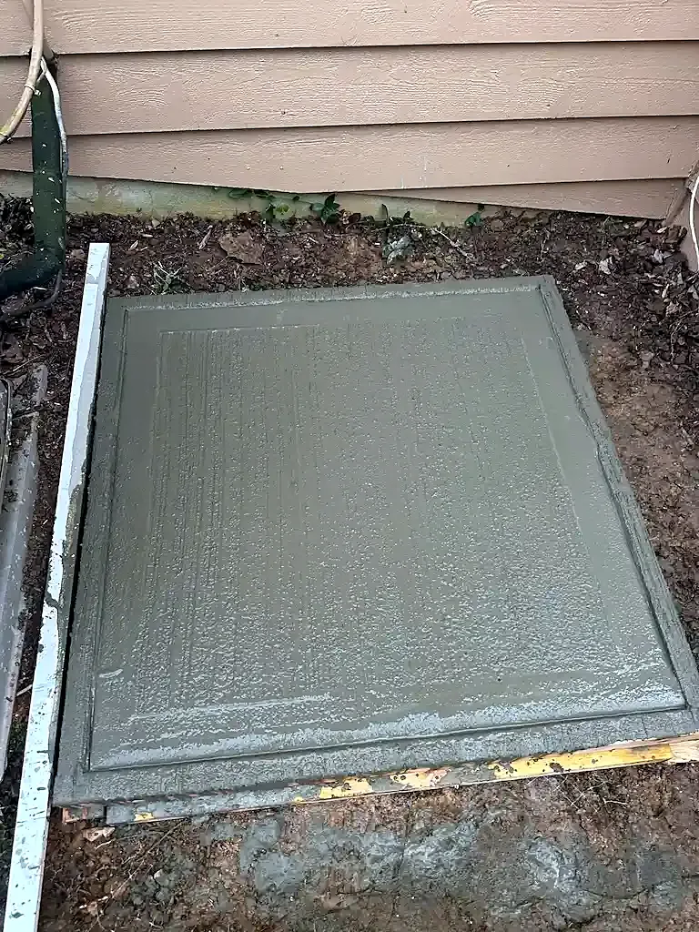 Cured gray concrete pad with a broom finish beside a house with tan siding