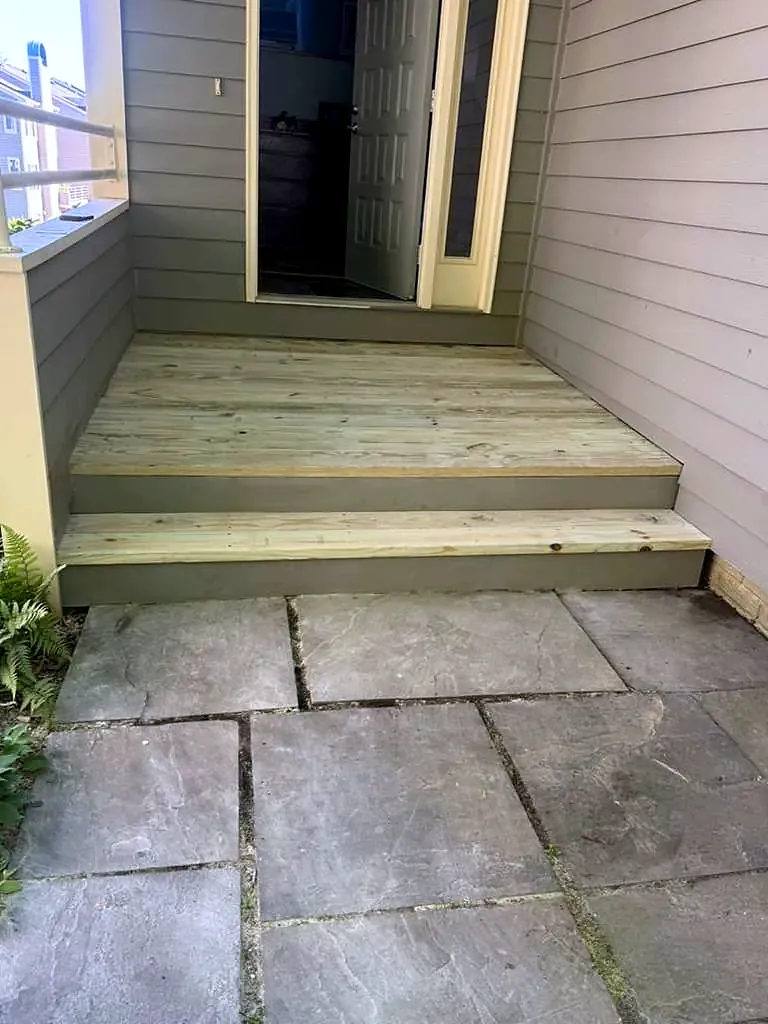 New pressure-treated wood landing and steps at a back door leading down to a flagstone patio