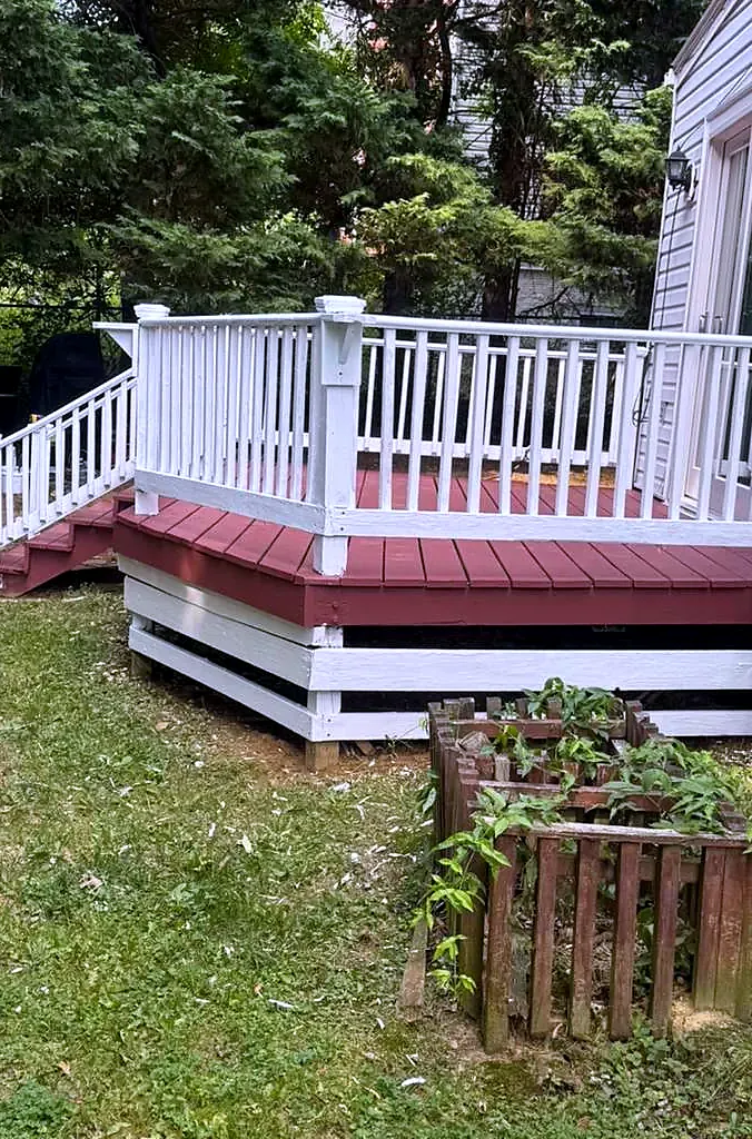 Red painted deck with white railing and white skirting beside a lawn and a small garden bed