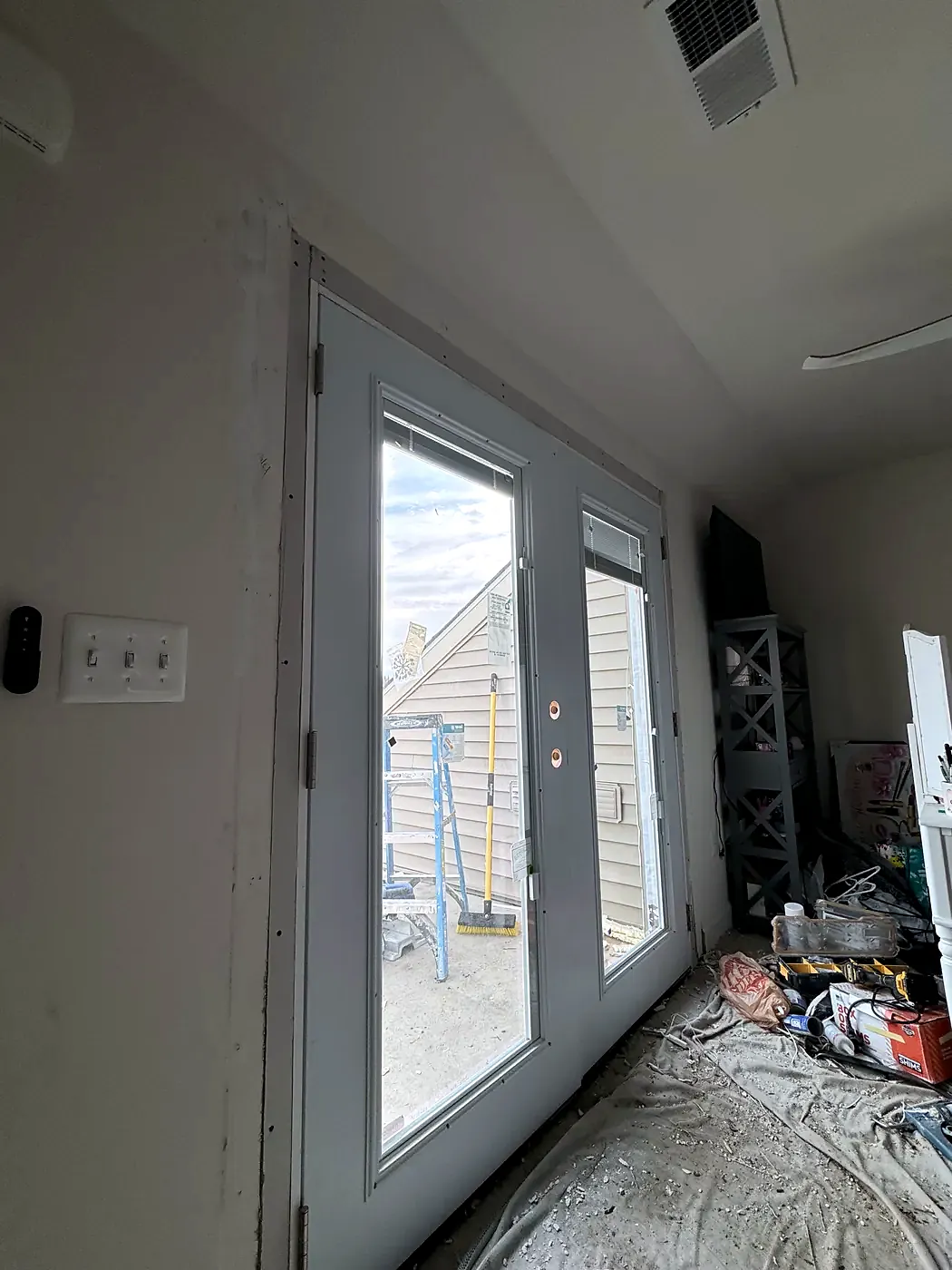 New white French doors installed in an attic room with a sloped ceiling, drop cloths and tools on the floor