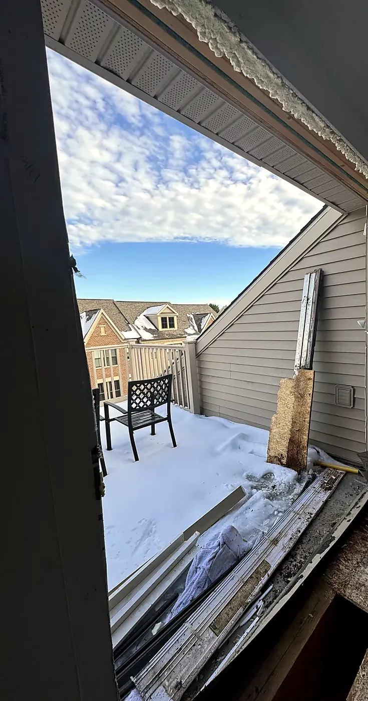 Rough door opening cut through a wall to a snow-covered roof deck with exposed framing and blue sky