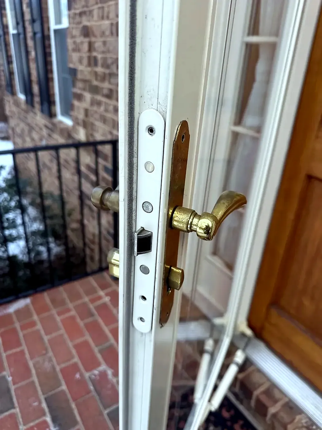 Edge of an open entry door showing a multipoint lock strip and brass lever handle, brick porch behind