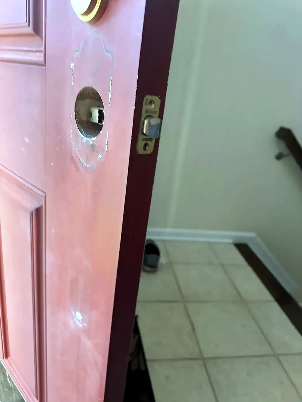 Red door with handle removed showing empty bore holes and patched filler, tile floor beyond