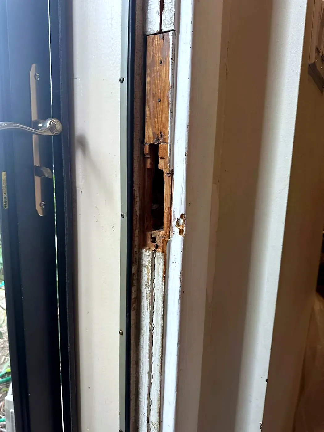 Peeling, rotted wood door jamb next to a dark blue storm door with a lever handle