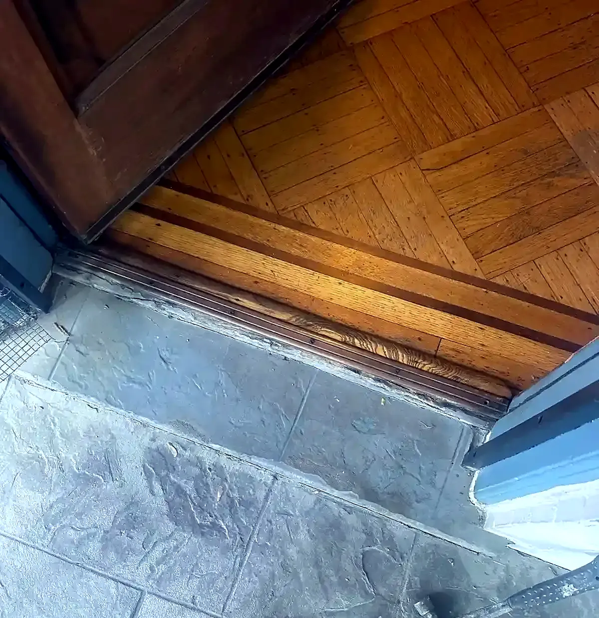 New wood threshold strip installed between parquet flooring and gray stone tile at the doorway