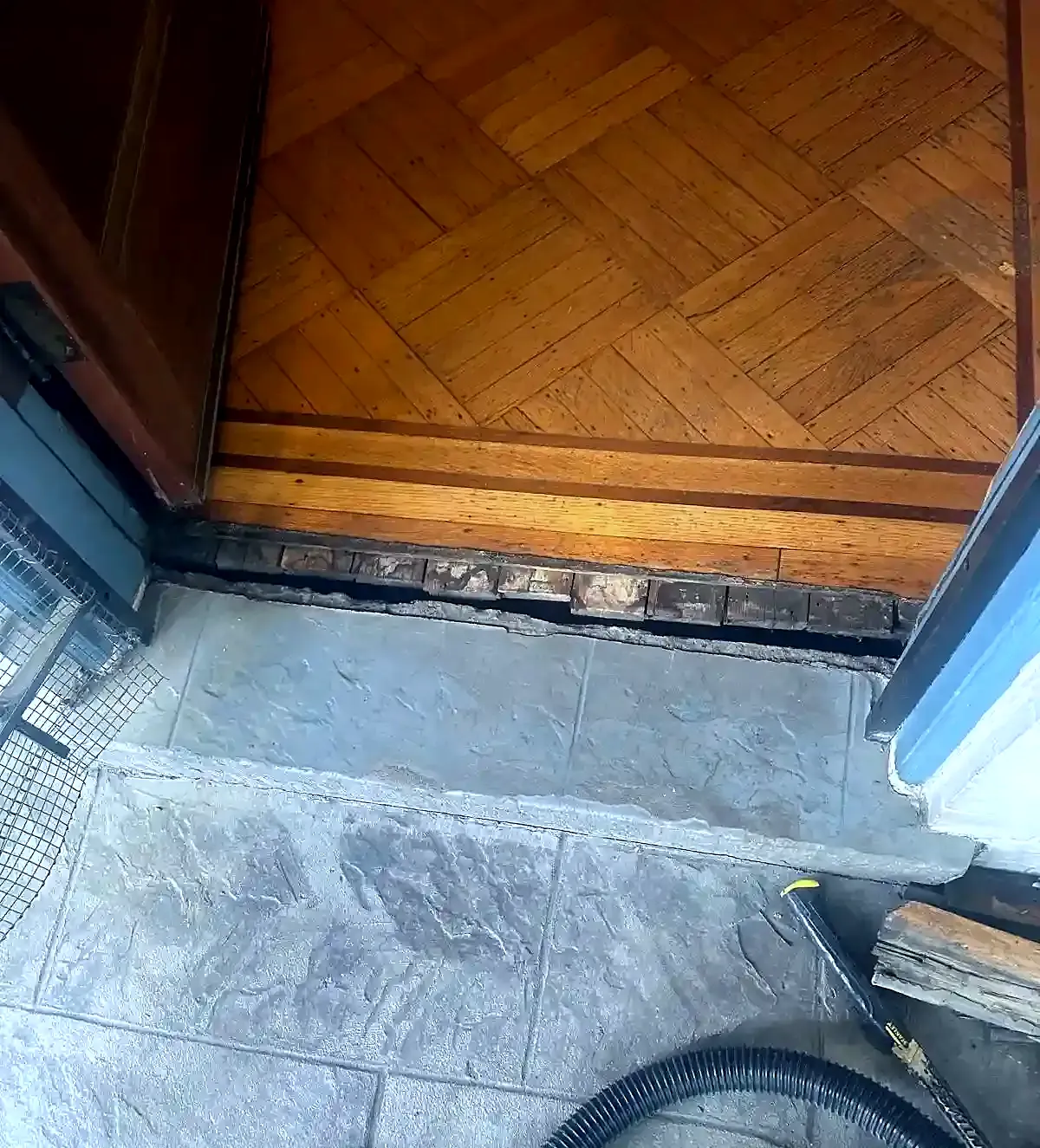 Rotted, gapped wood threshold between a parquet floor and gray stone tile at an open door
