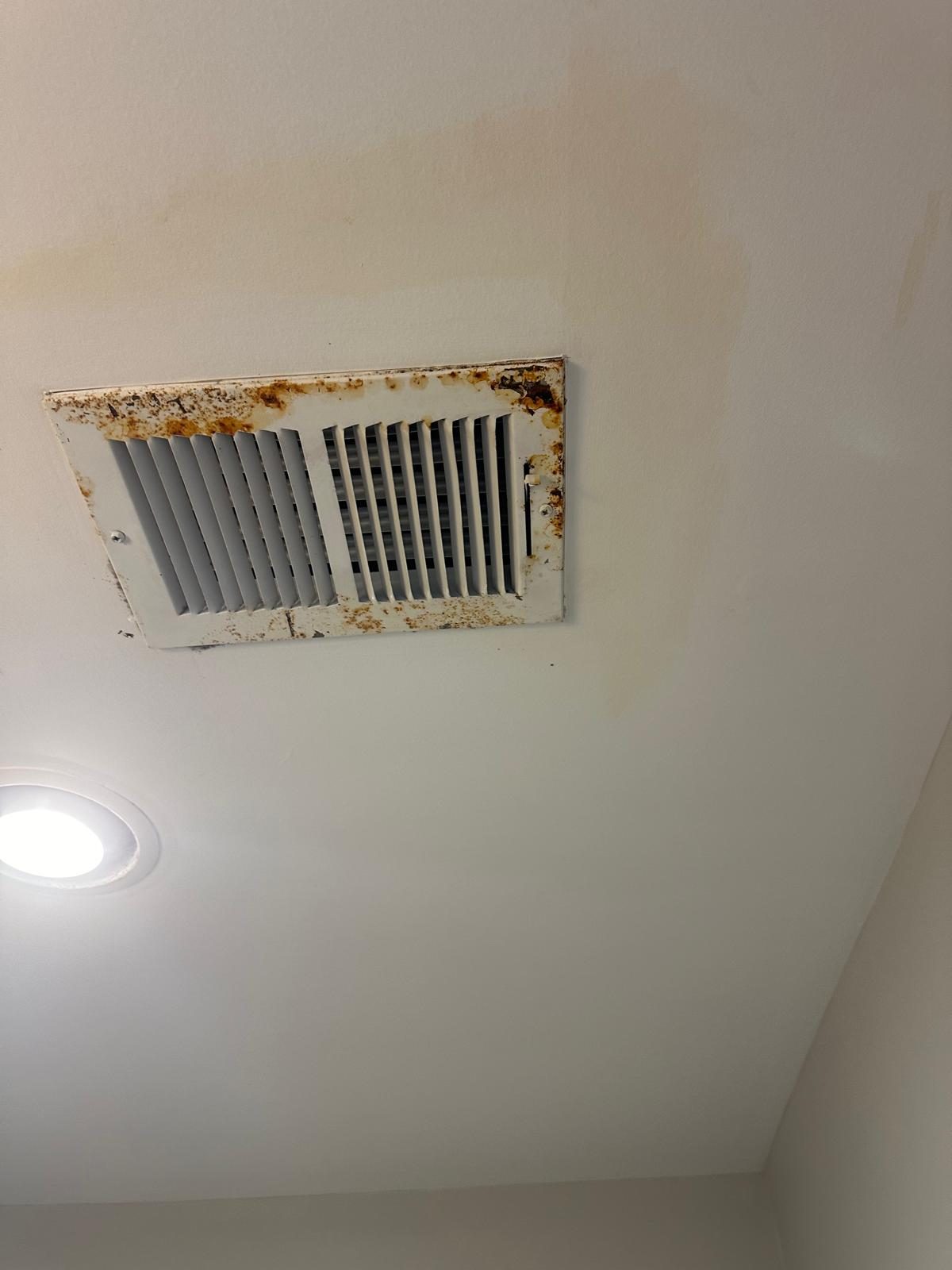 Rusted ceiling vent surrounded by brown water staining on the drywall