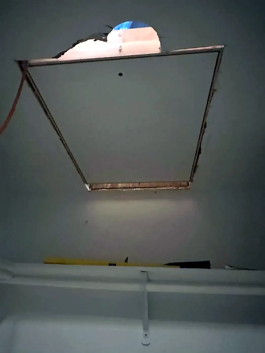 Rough attic hatch opening in a ceiling with damaged drywall edges and exposed wood framing