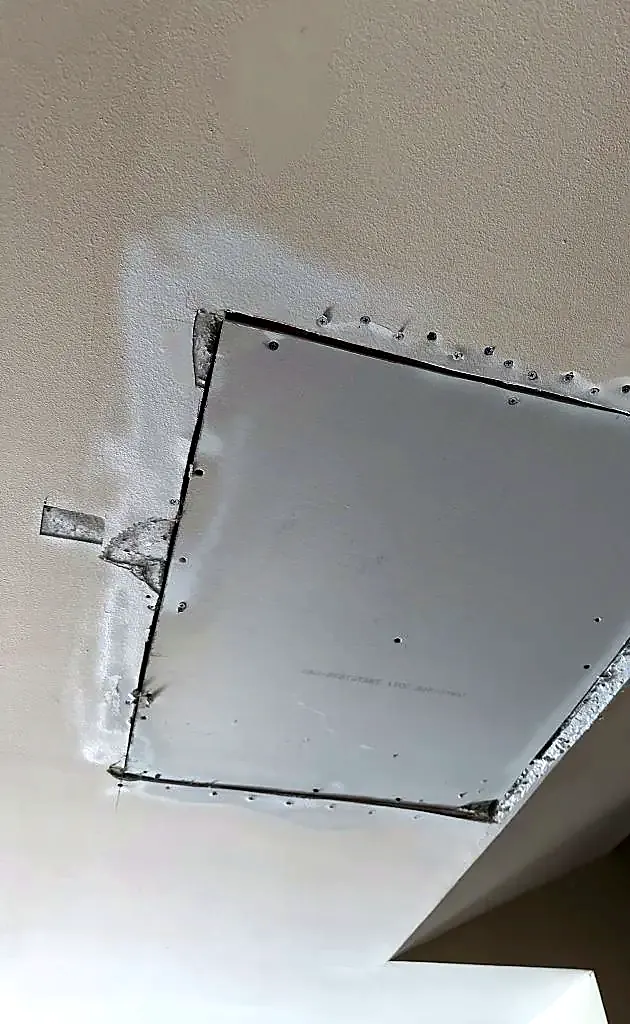 New rectangular drywall patch screwed into a ceiling with fresh joint compound around the edges