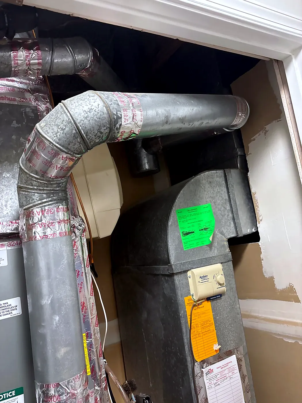 Round galvanized ducts and a humidifier bypass duct sealed with foil tape above a furnace plenum with labels