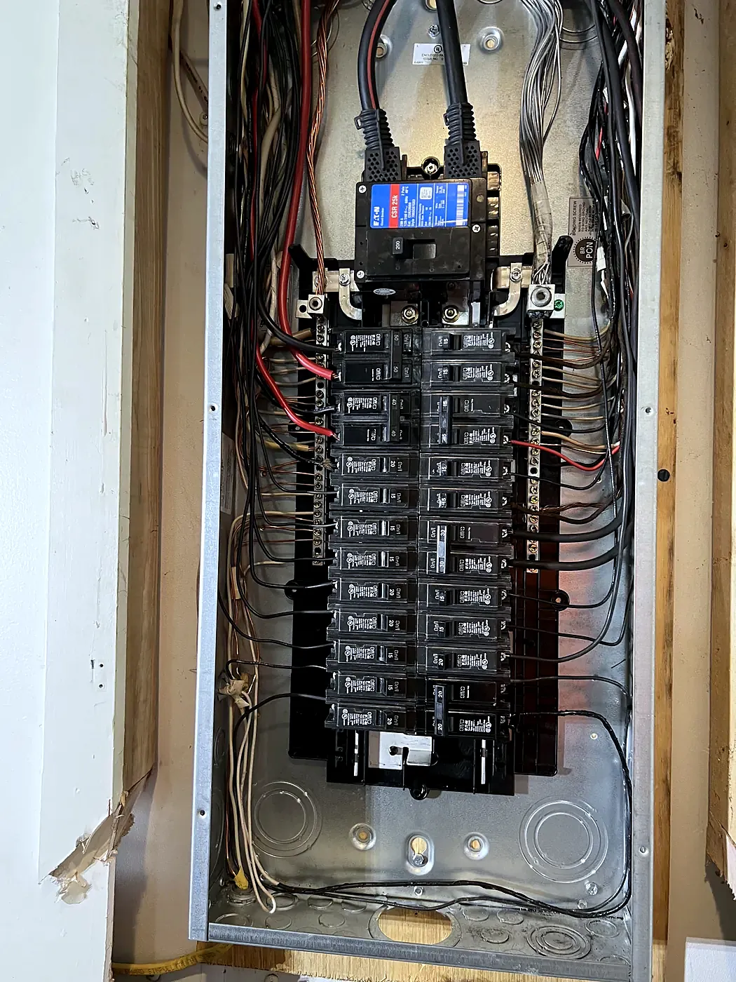 Open electrical panel with main breaker on top and two full columns of black breakers, wires routed along the sides