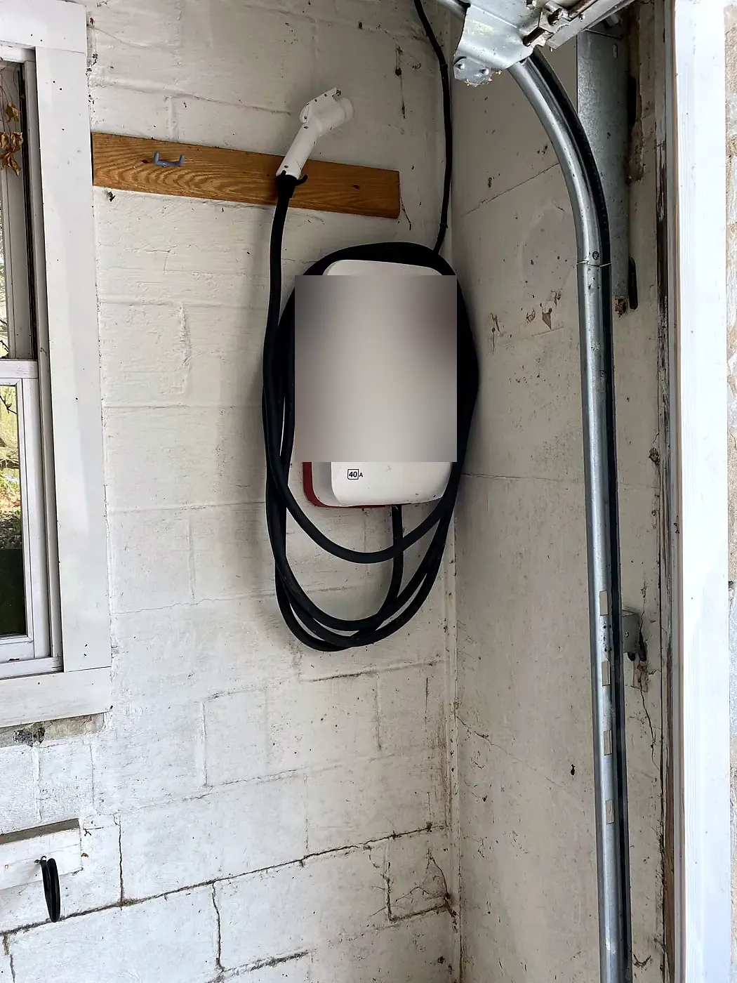 White EV charger mounted on a painted white cinderblock garage wall with the cable coiled