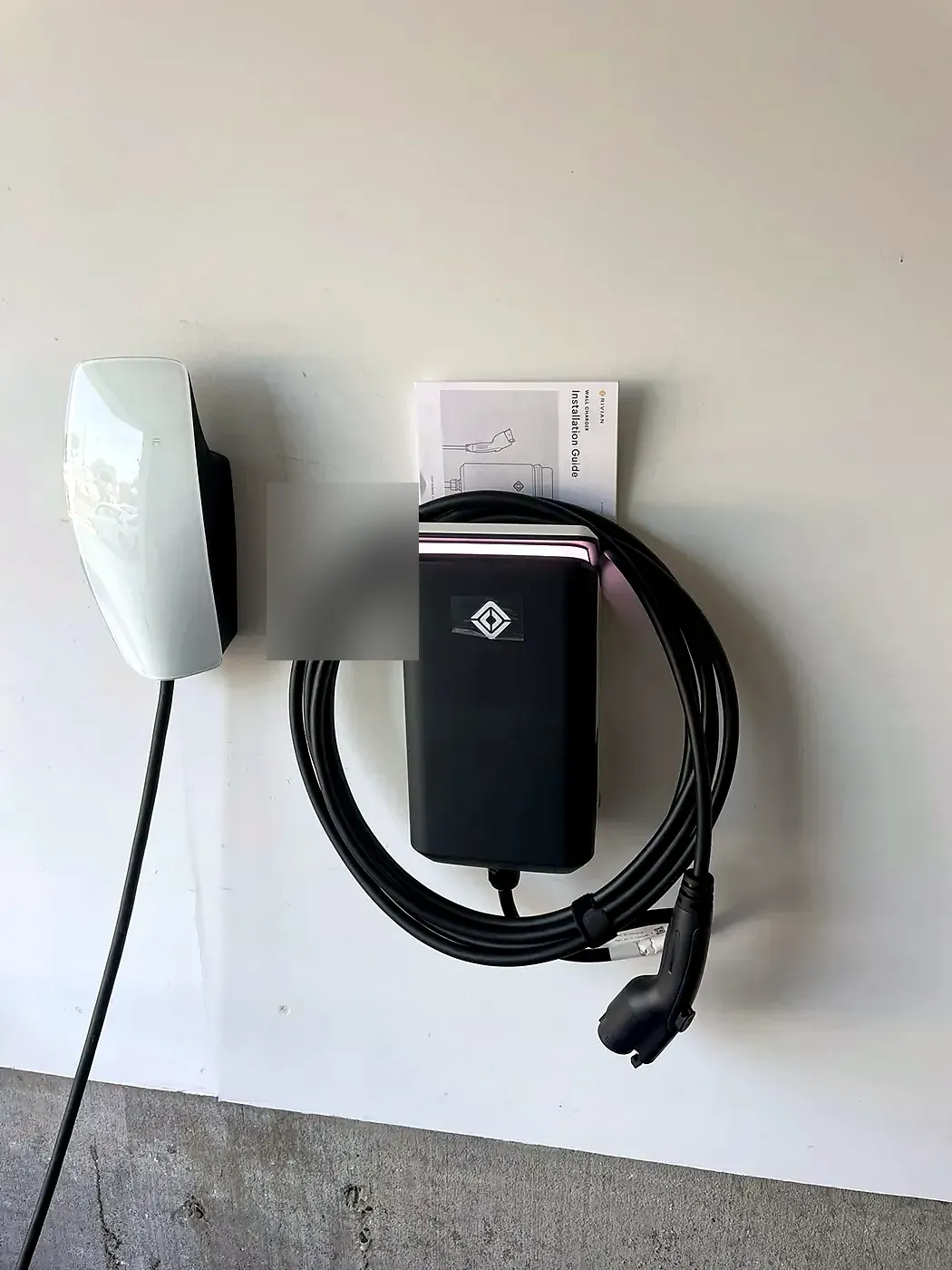White EV charging unit on a white wall with a black cable coiled beneath and connector holstered