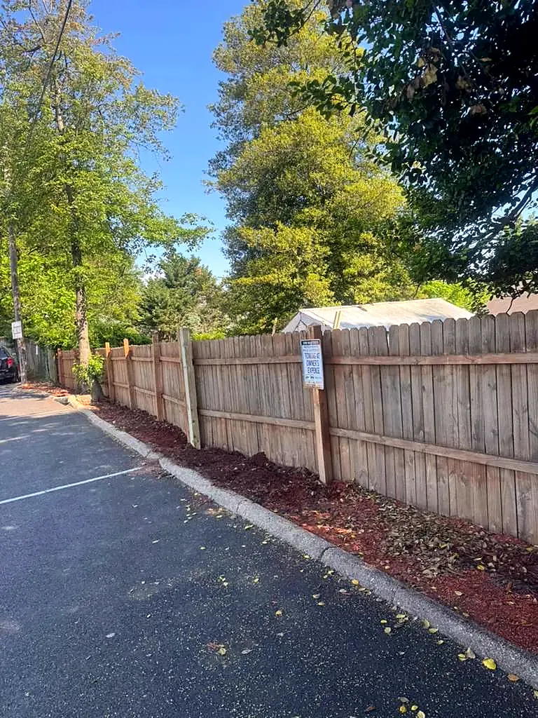 Tall wood privacy fence running along the edge of an asphalt parking lot under trees