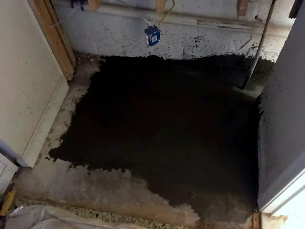 Wet, freshly troweled gray concrete patch on a basement floor next to white walls and wood framing