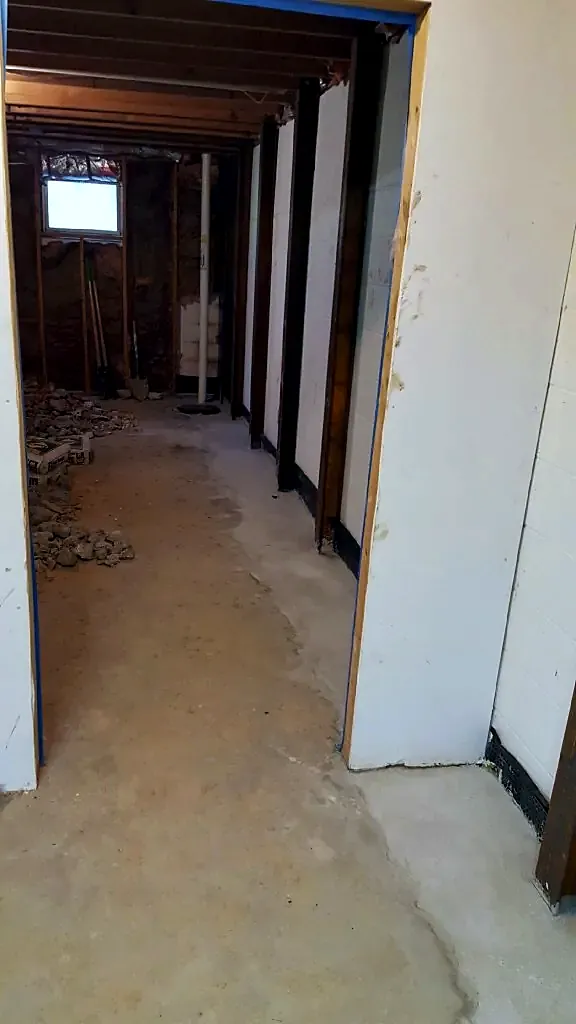 Basement hallway with white wall panels and a fresh gray concrete patch along the floor edge