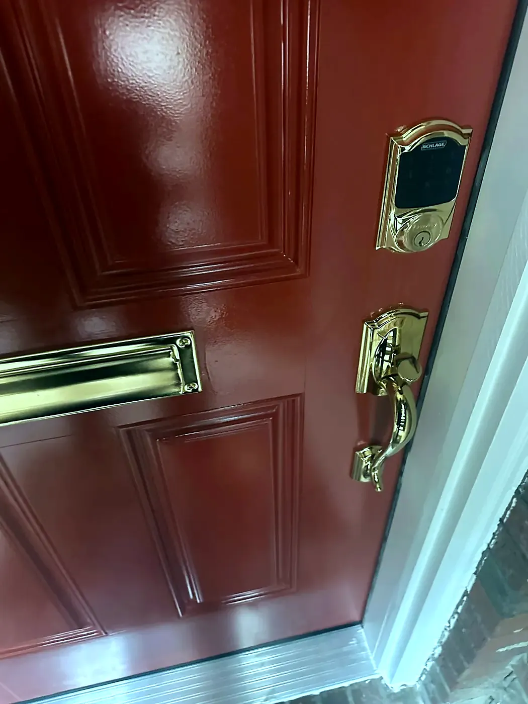 Red six-panel door with brass mail slot, brass handleset, and a keypad smart deadbolt