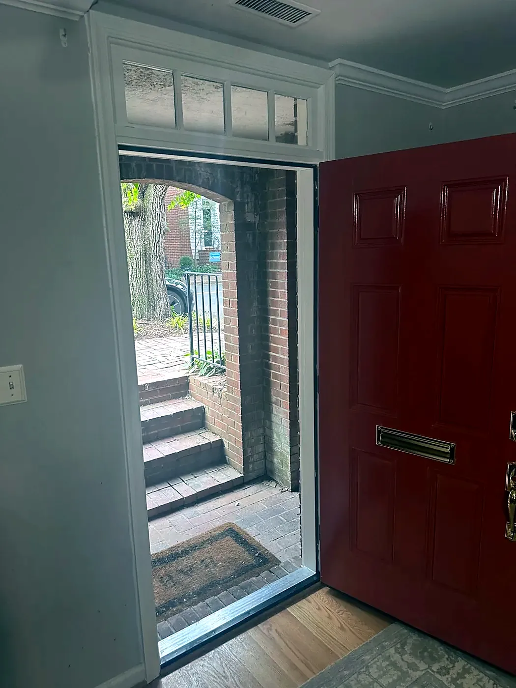 Open red front door seen from a foyer, transom window above and brick steps outside