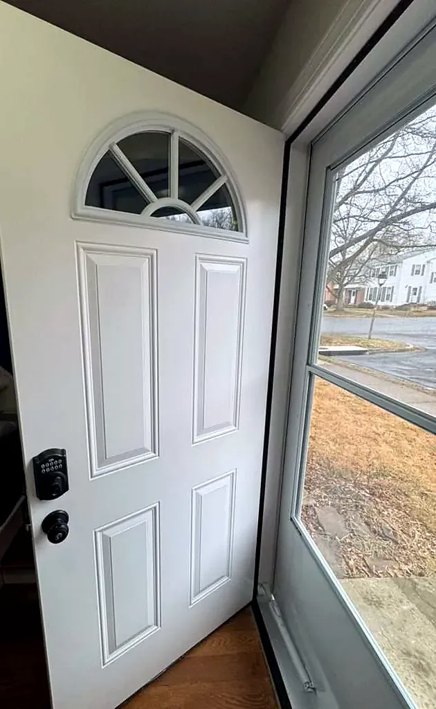 White fanlight front door open at an angle toward the yard, black keypad lock on the edge