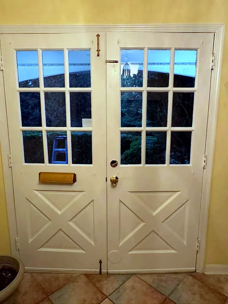 Old cream double entry doors with small glass panes and cross-buck lower panels, seen from inside