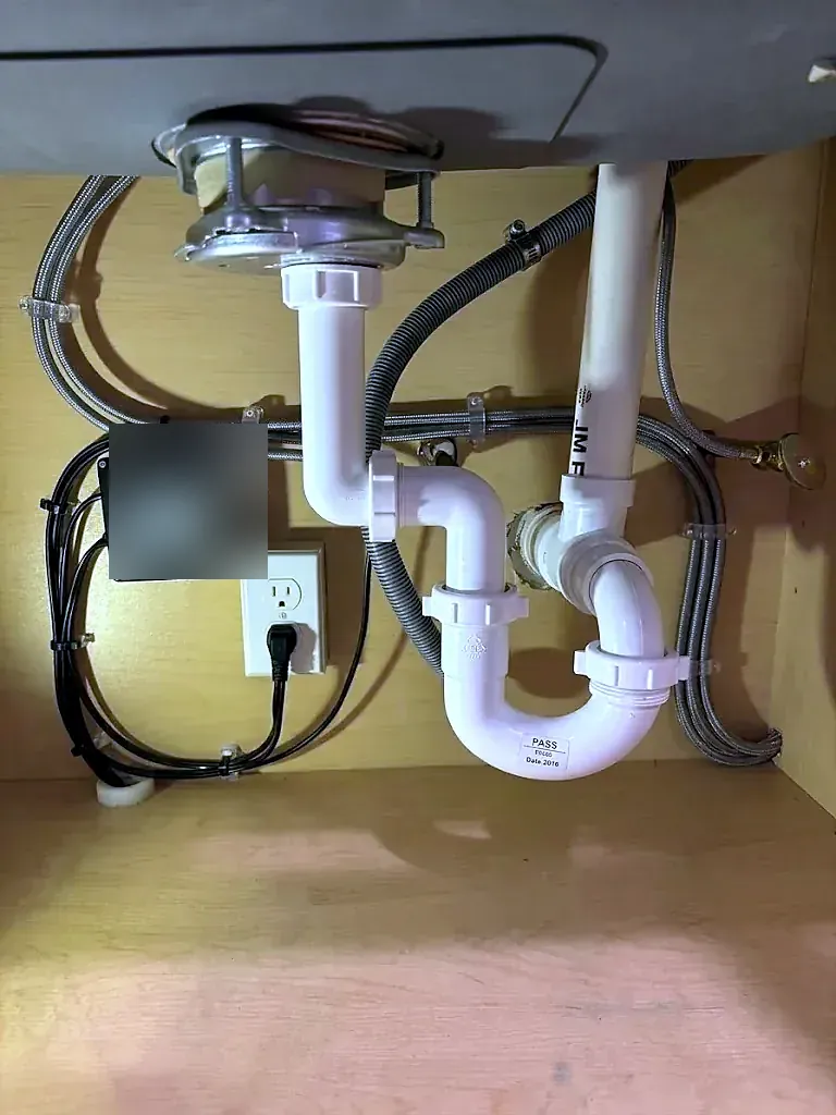 Under-sink cabinet with a garbage disposal, white PVC P-trap, braided hoses and an outlet