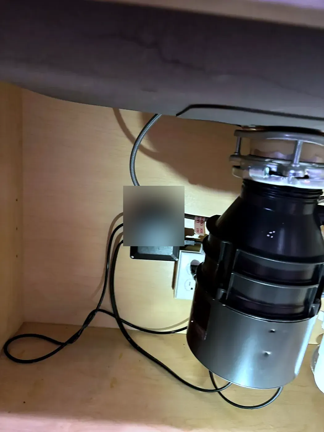 Garbage disposal mounted under a sink with a control box and power cord plugged into a wall outlet