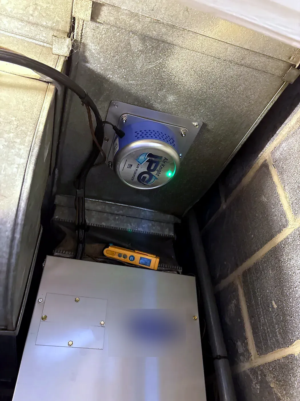 Furnace in a small closet with flue pipe and an air purifier mounted in the duct above