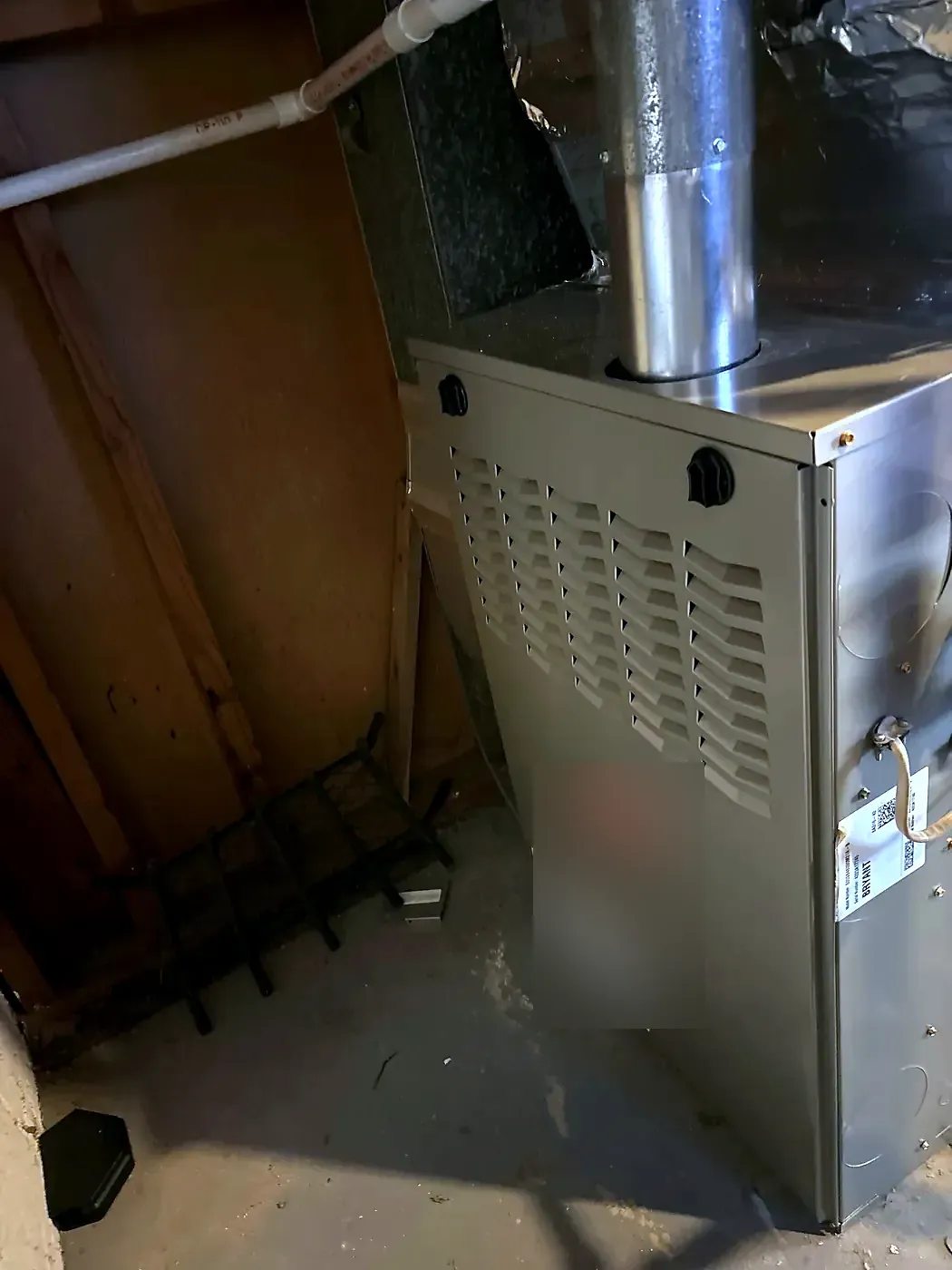 Gray furnace in a basement closet with a metal flue pipe rising from the top