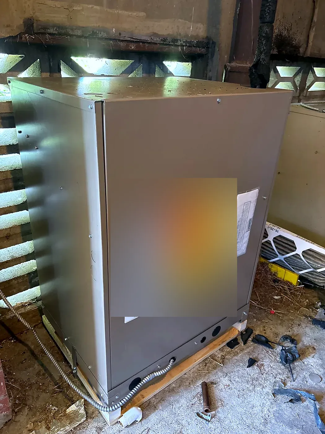 New gray furnace on a wood stand in a basement, yellow EnergyGuide label on the front