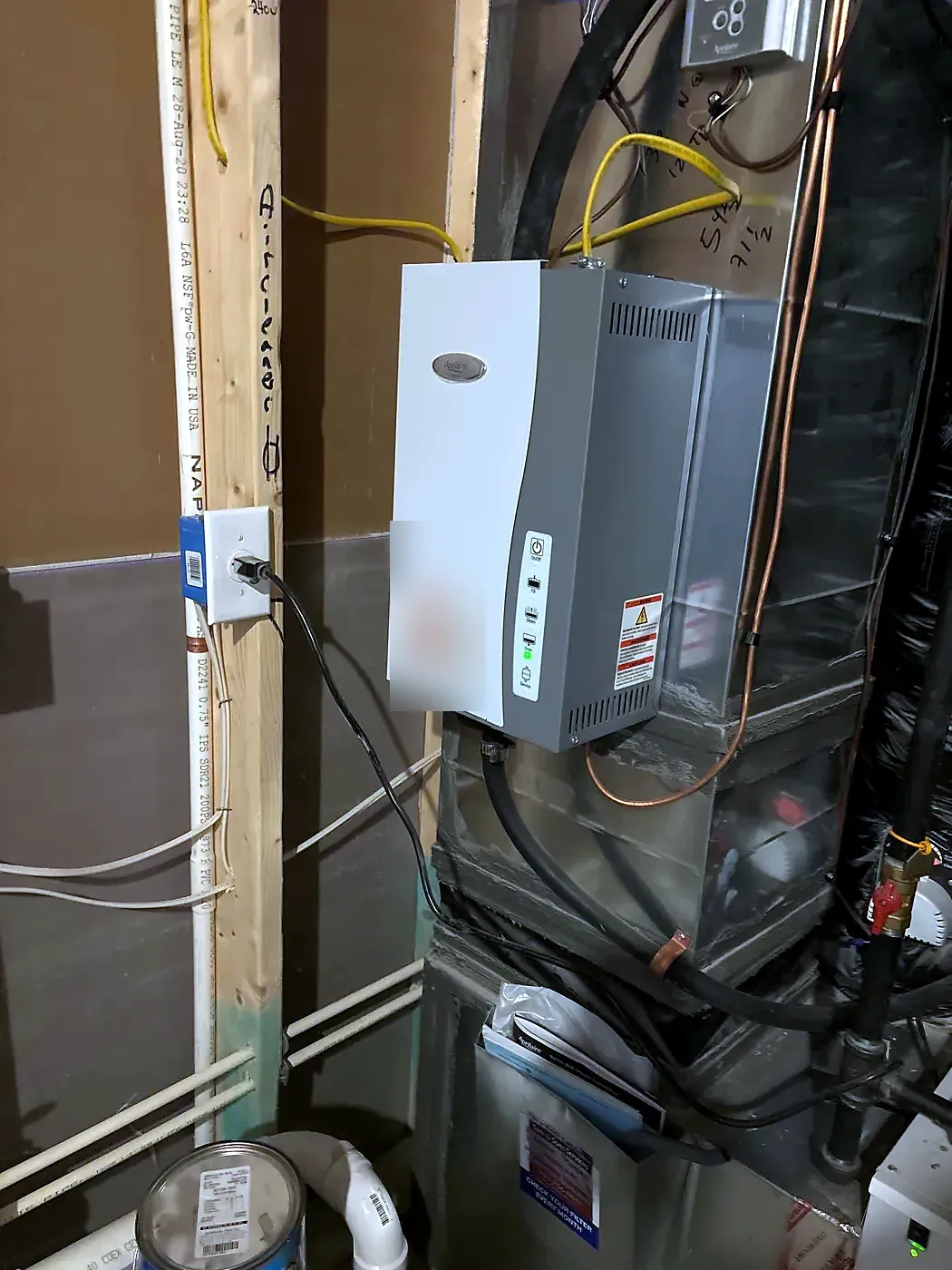 Furnace cabinet with a wall-mounted humidifier above it and condensate tubing running to the floor