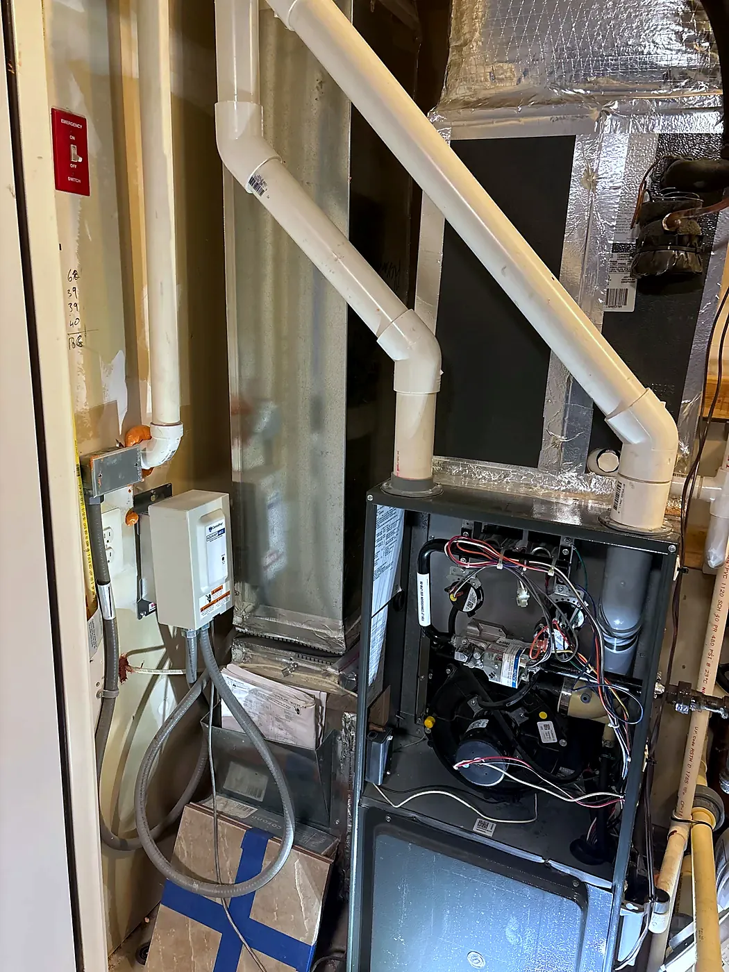 Furnace in a closet with lower panel off, white PVC vent pipes rising above it