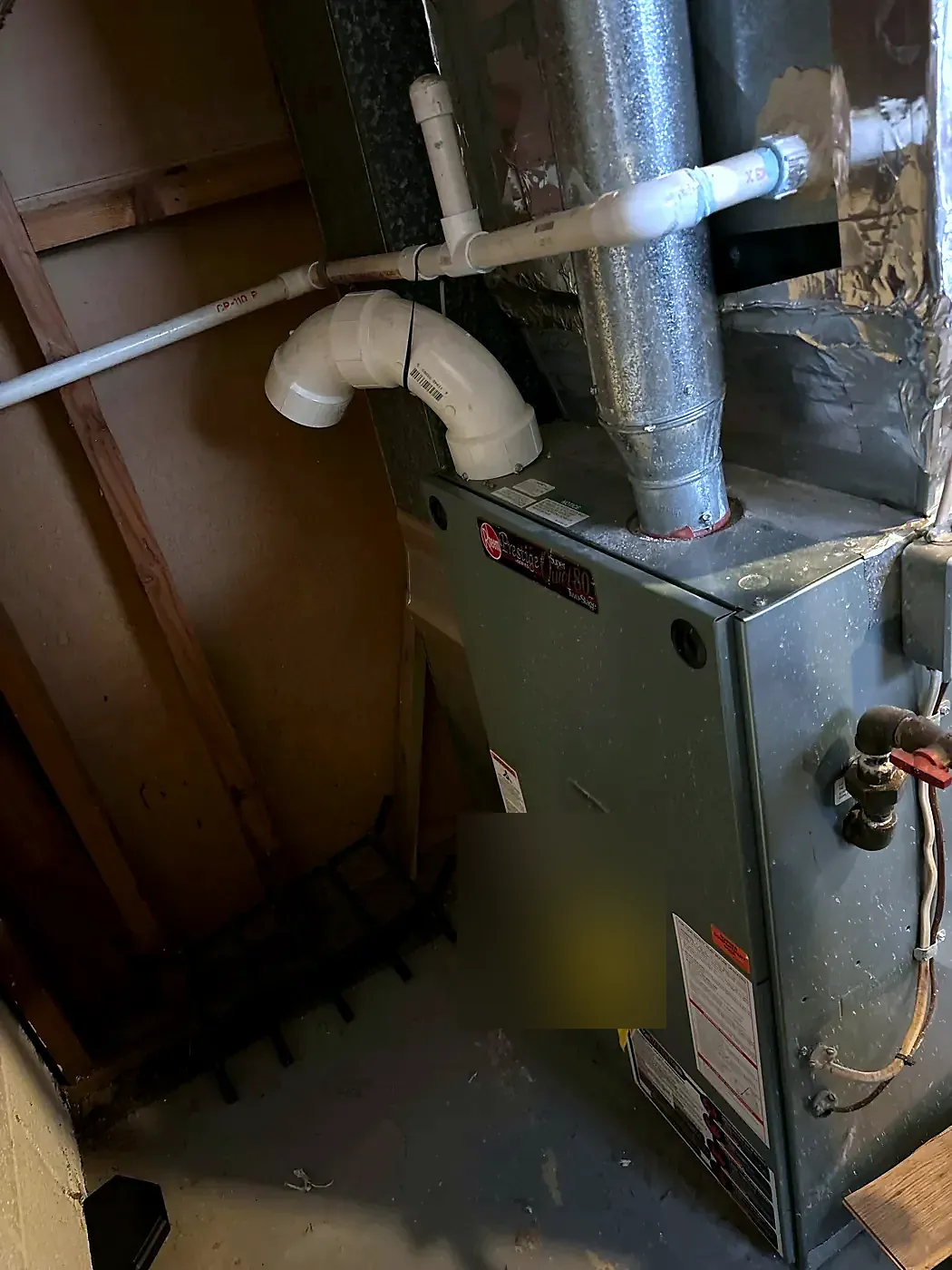 Gray furnace in an unfinished basement with white PVC vent pipe and copper lines above