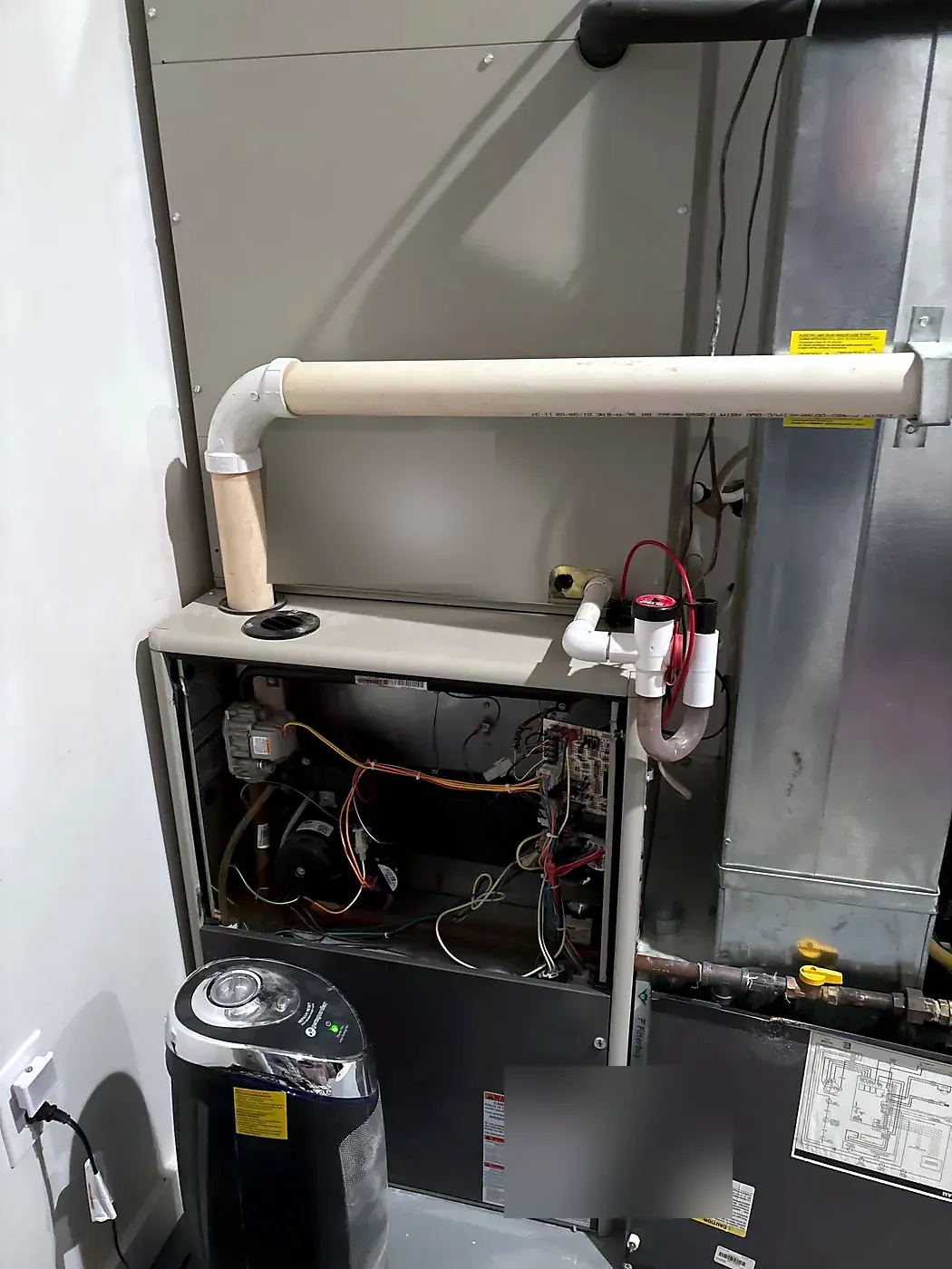 Furnace with front cover removed, condensate pump on the floor and PVC flue pipe above
