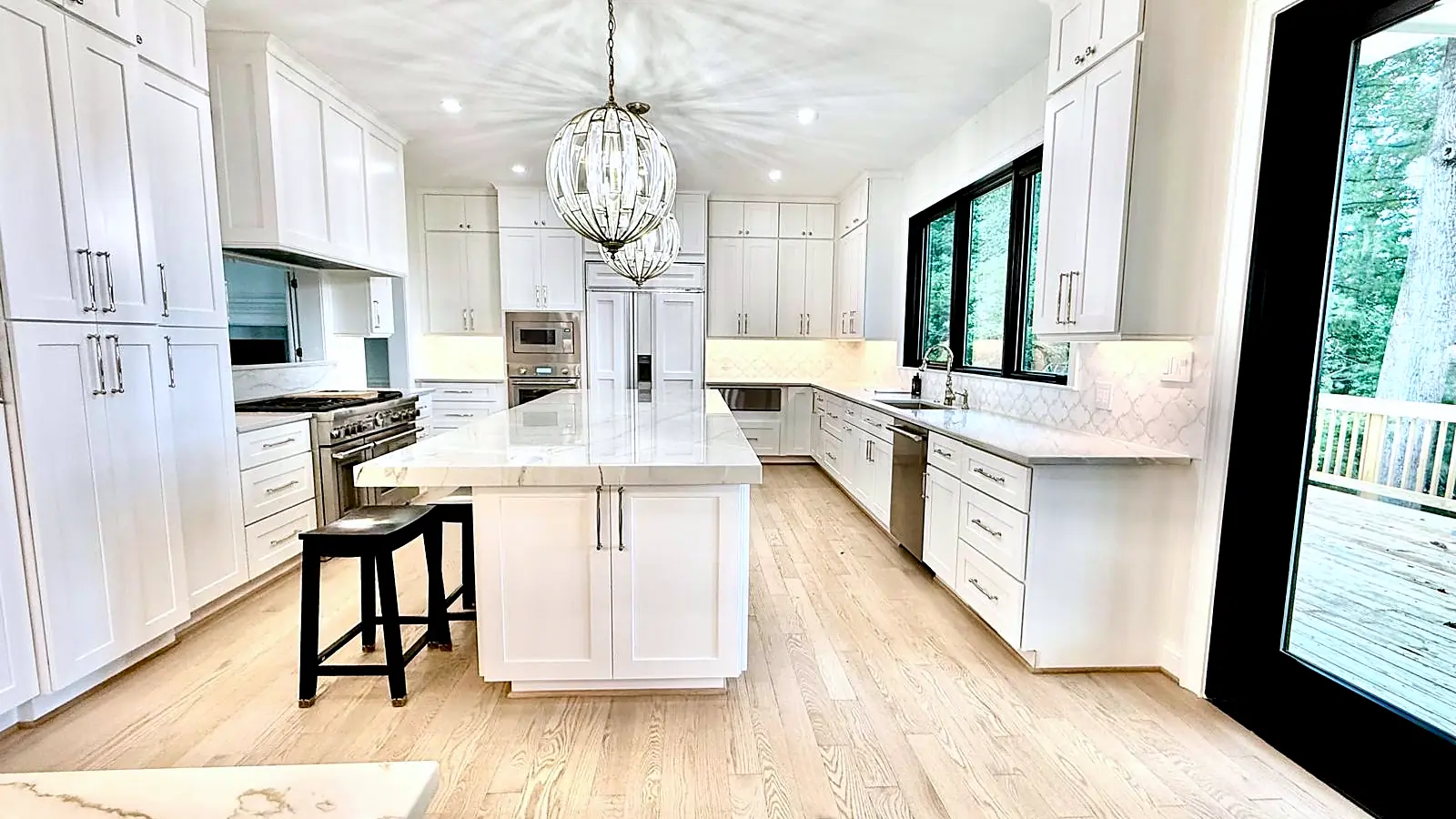 Finished kitchen remodel by Sam & Sons Services with white cabinets, marble island and wide-plank floor