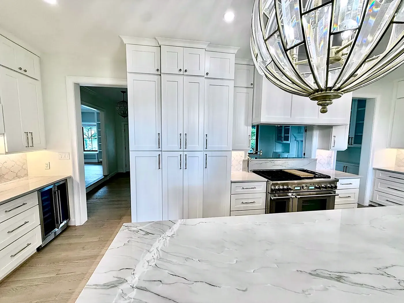 Marble-look island top under a caged globe pendant with white cabinets and a stainless range behind