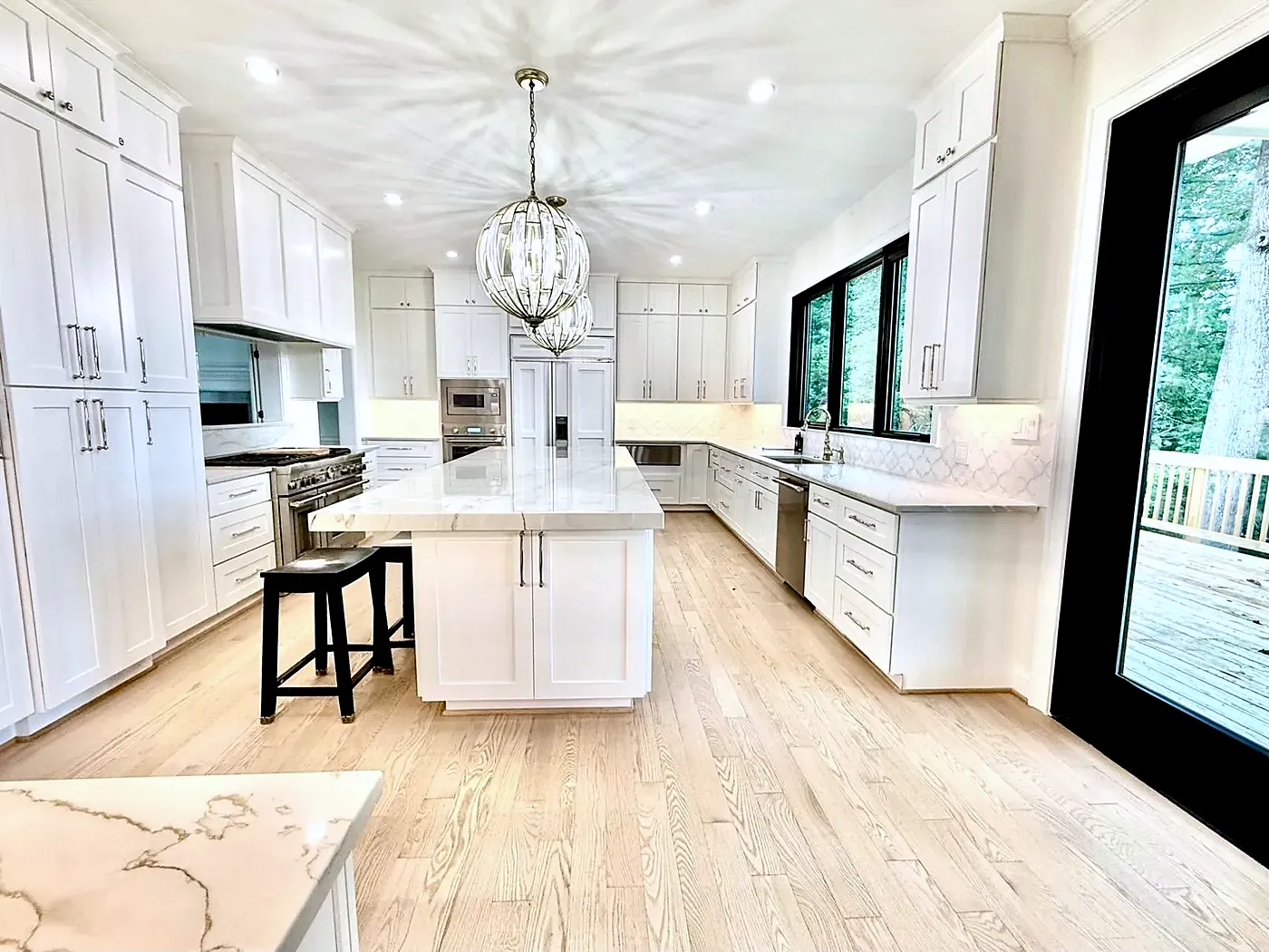 White kitchen with an island and stool, globe pendant, black-framed windows and light wood floor